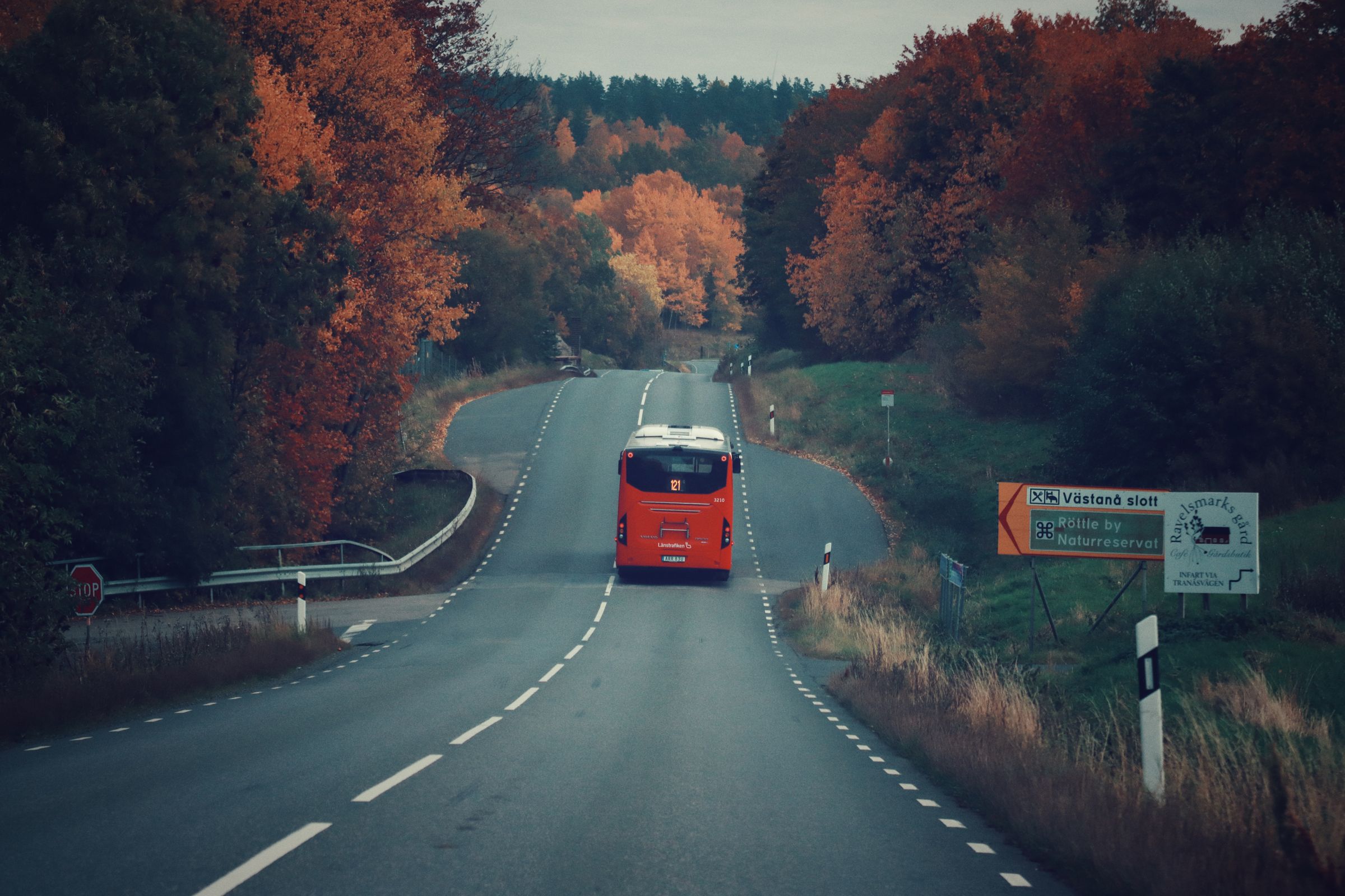 Röd Länstrafiken-buss på en svensk landsväg genom höstfärgad skog