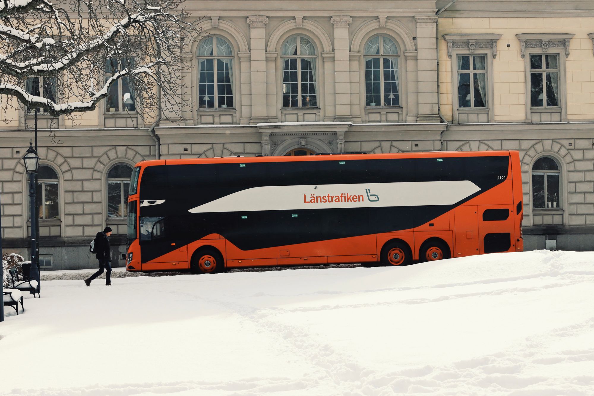 Orange Länstrafiken-dubbeldäckare parkerad vid ett snötäckt torg en vinterdag
