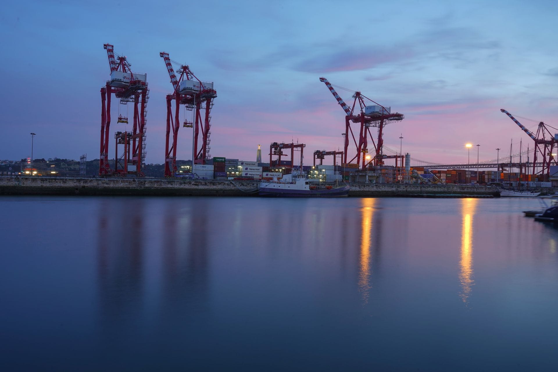 Containerhamn i skymning med höga kranar som speglas i vattnet