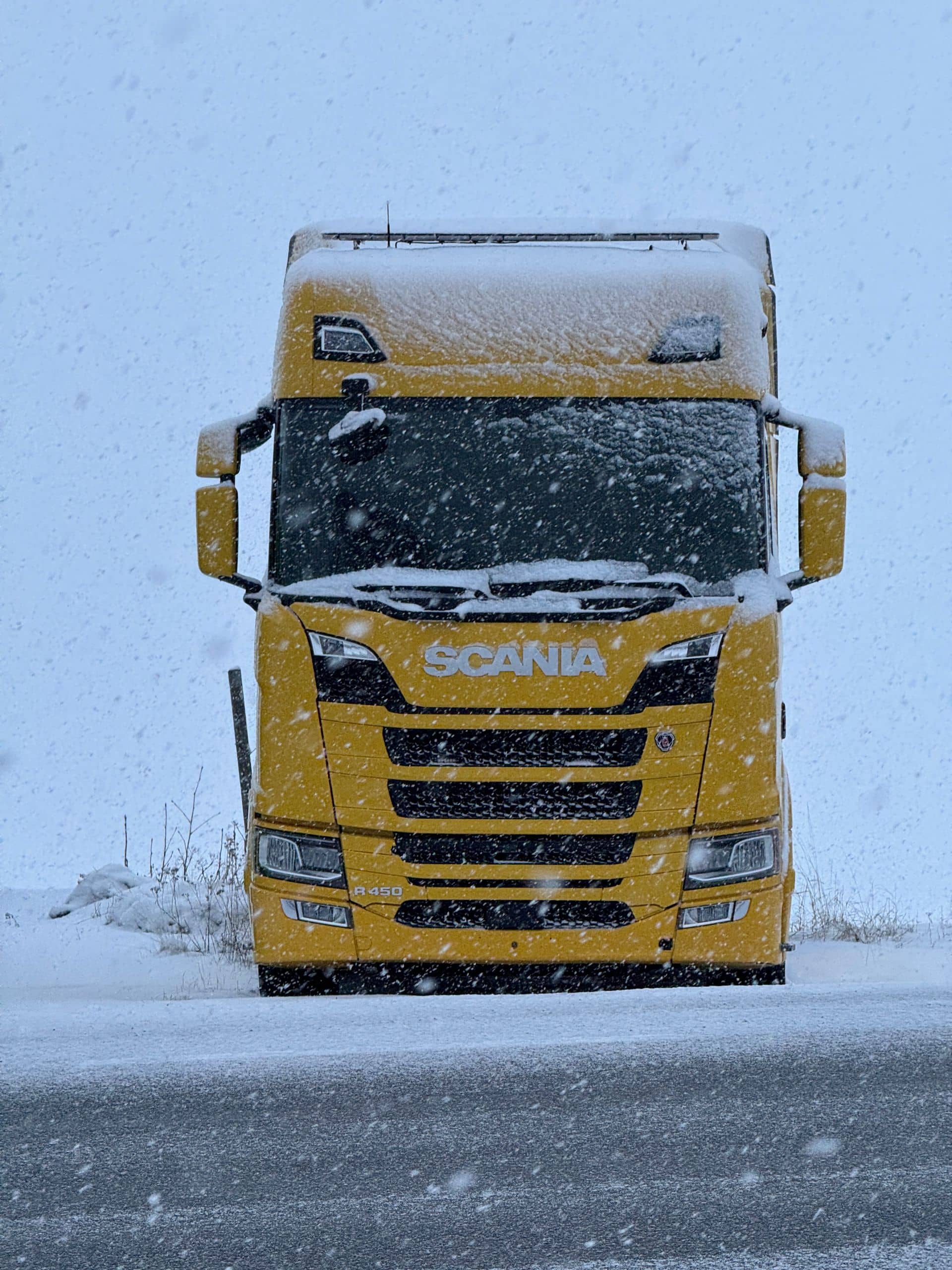 Gul Scania-lastbil rakt framifrån på en snöig plats