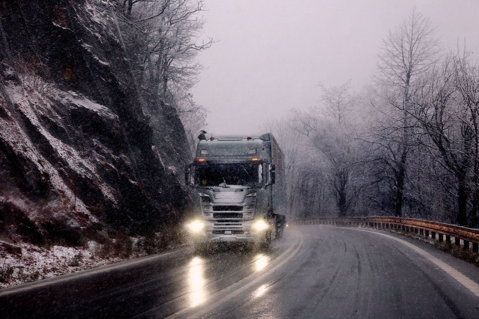 Lastbil med tända strålkastare på en snöig, dimmig skogsväg
